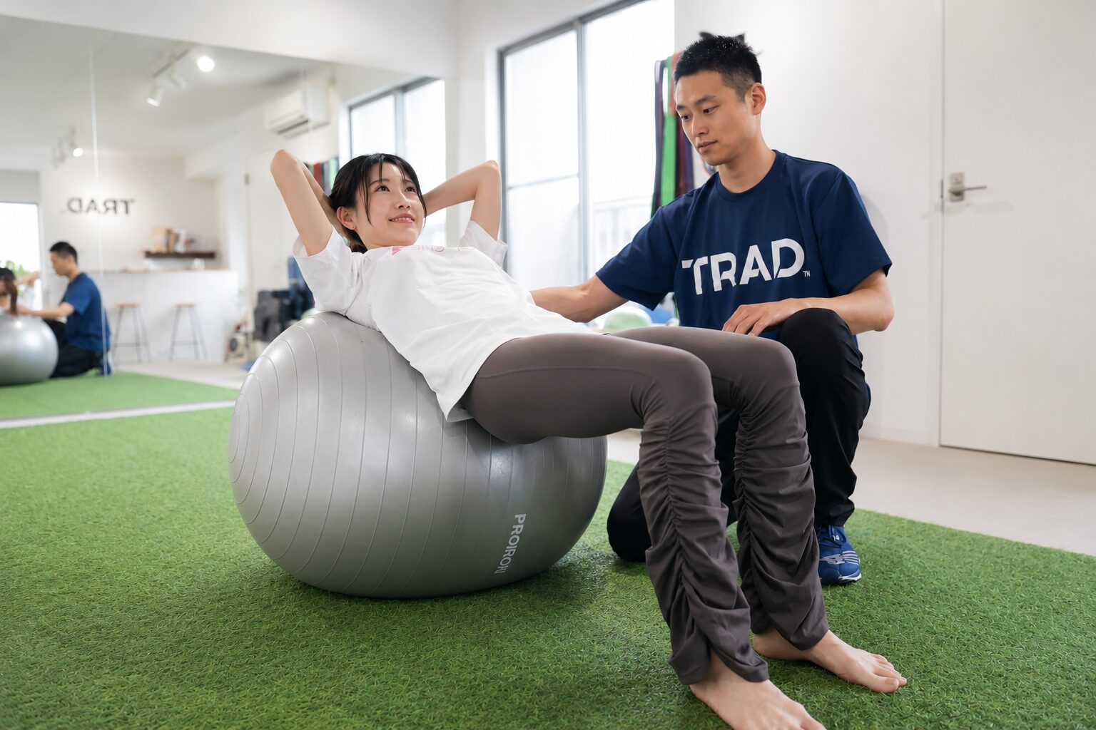 トレーナーがバランスボールで体幹トレーニングを丁寧に指導する様子｜東海市のパーソナルジムTRAD